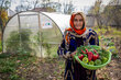 A woman holding a basket of peppers, parsley and green onions.
